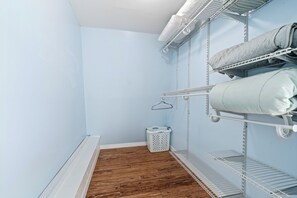 A laundry room with metal shelves, a wooden floor, and a white laundry basket. - Spacious two-story 2BR, 3-bath beachside condo with a private patio and upstairs balcony. Just a short drive, bike or golf cart ride to the beach. (New Smyrna Beach)