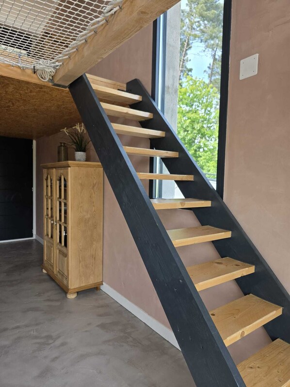 A modern staircase with wooden steps and black railings, leading to a room with a large window and a wooden cabinet.