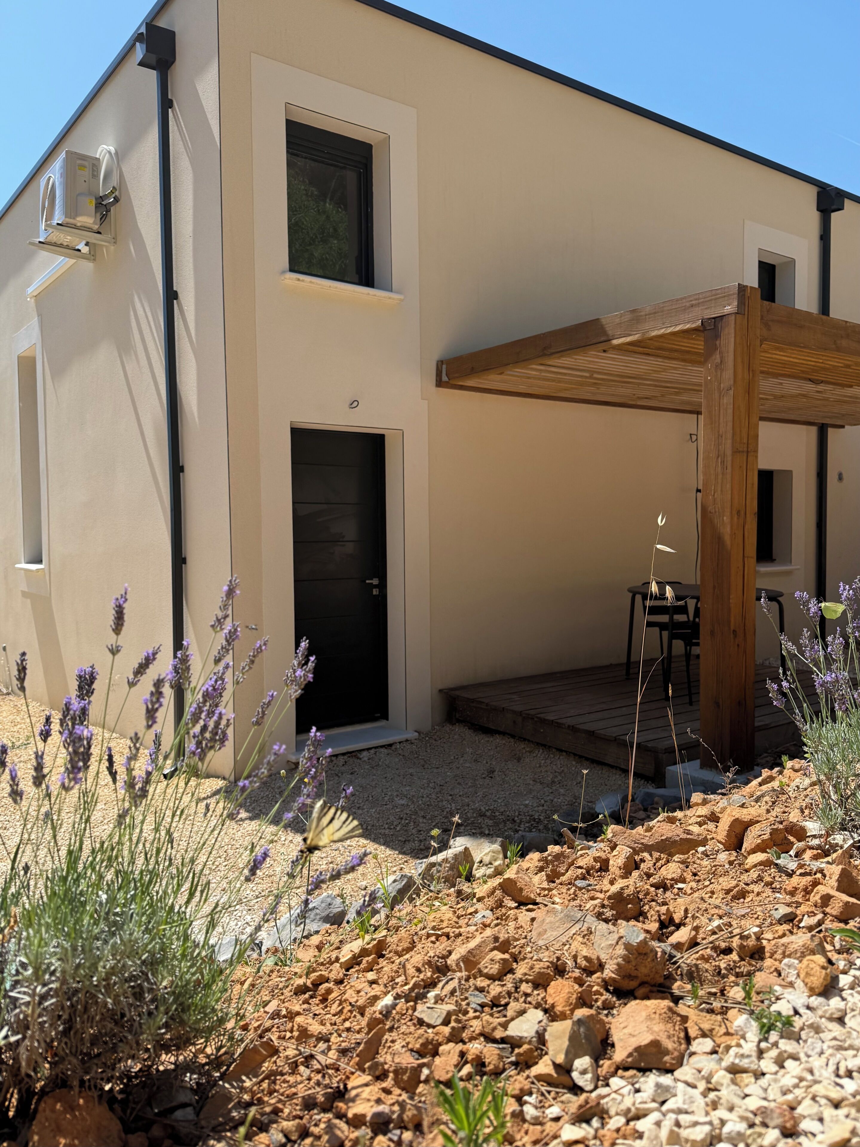 Ein modernes Gebäude mit einer schwarzen Tür, einem kleinen Fenster und einer Holz-Pergola.