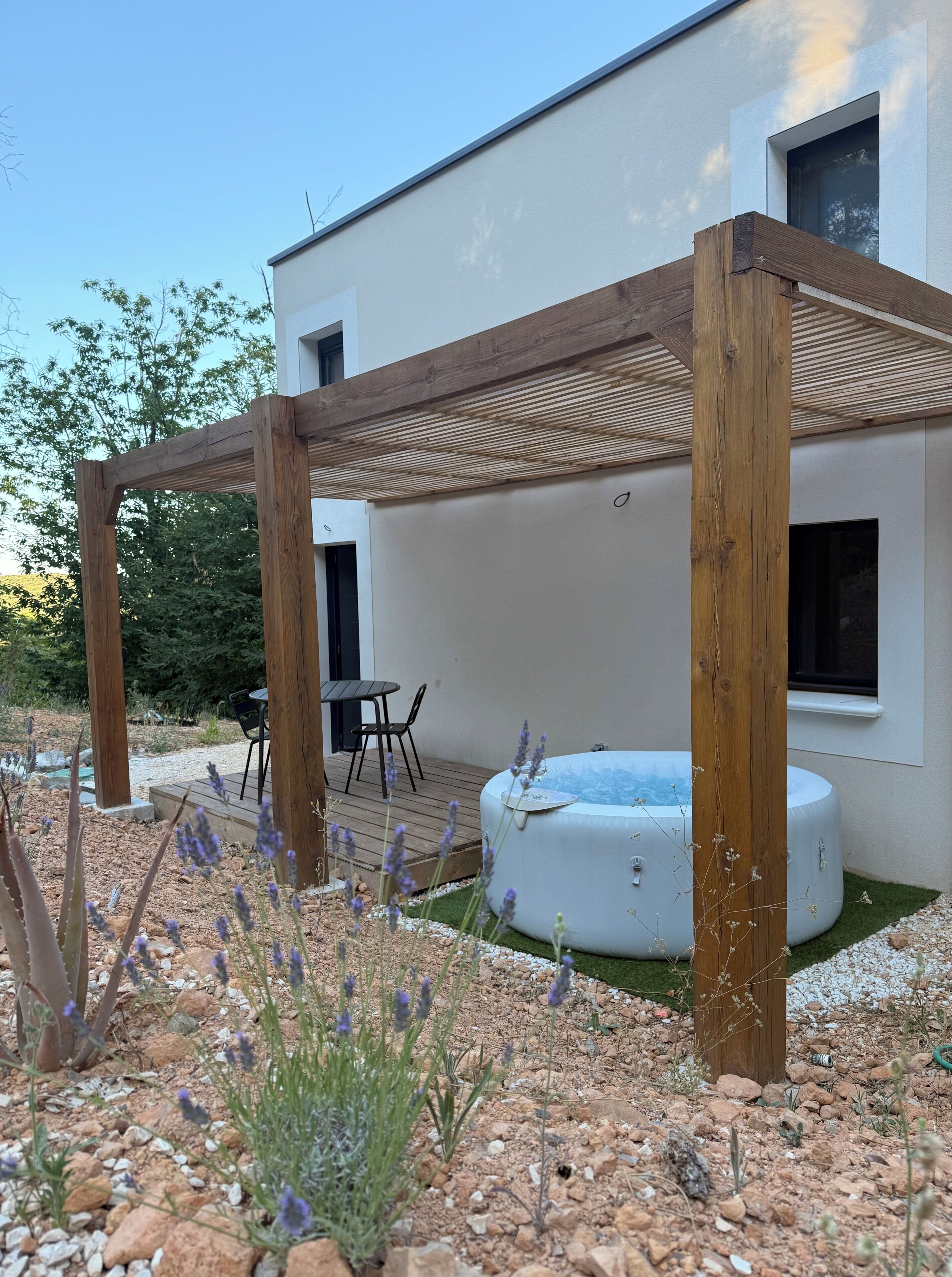 En moderne udendørs terrasse med et træbeklædt pergola, et spabad og et siddeområde med bord og stole.