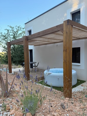 A modern outdoor patio with a wooden pergola, a hot tub, and a seating area with a table and chairs.