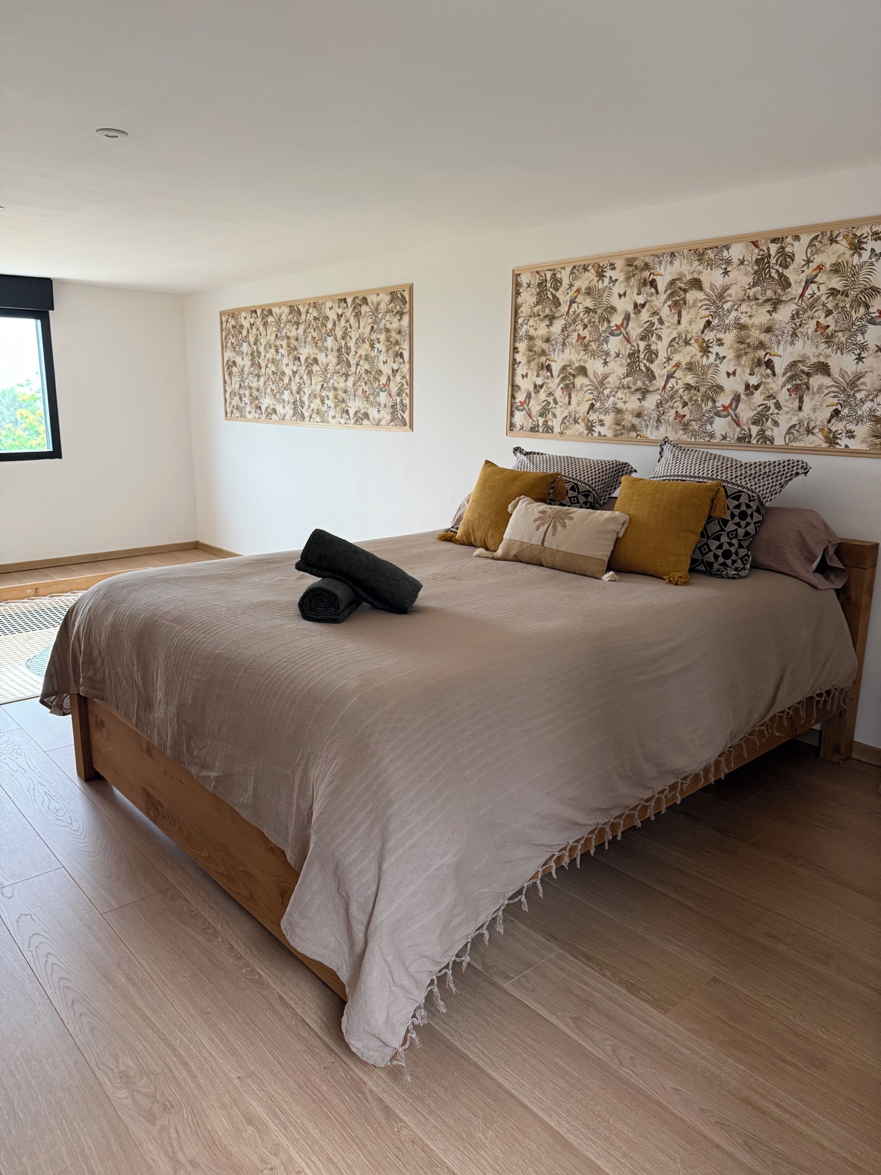 Een slaapkamer met een groot bed, een raam en twee kunstwerken aan de muur.