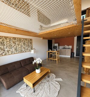 A modern living room with a sofa, a wooden coffee table, and a dining area with a table and chairs. - The Hanging Nest & SPA (Saint-Martin-de-Valgalgues)