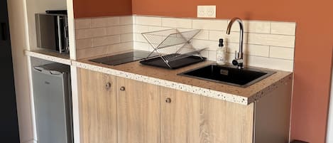 A kitchen with a countertop, sink, cabinets, and a trash bin.