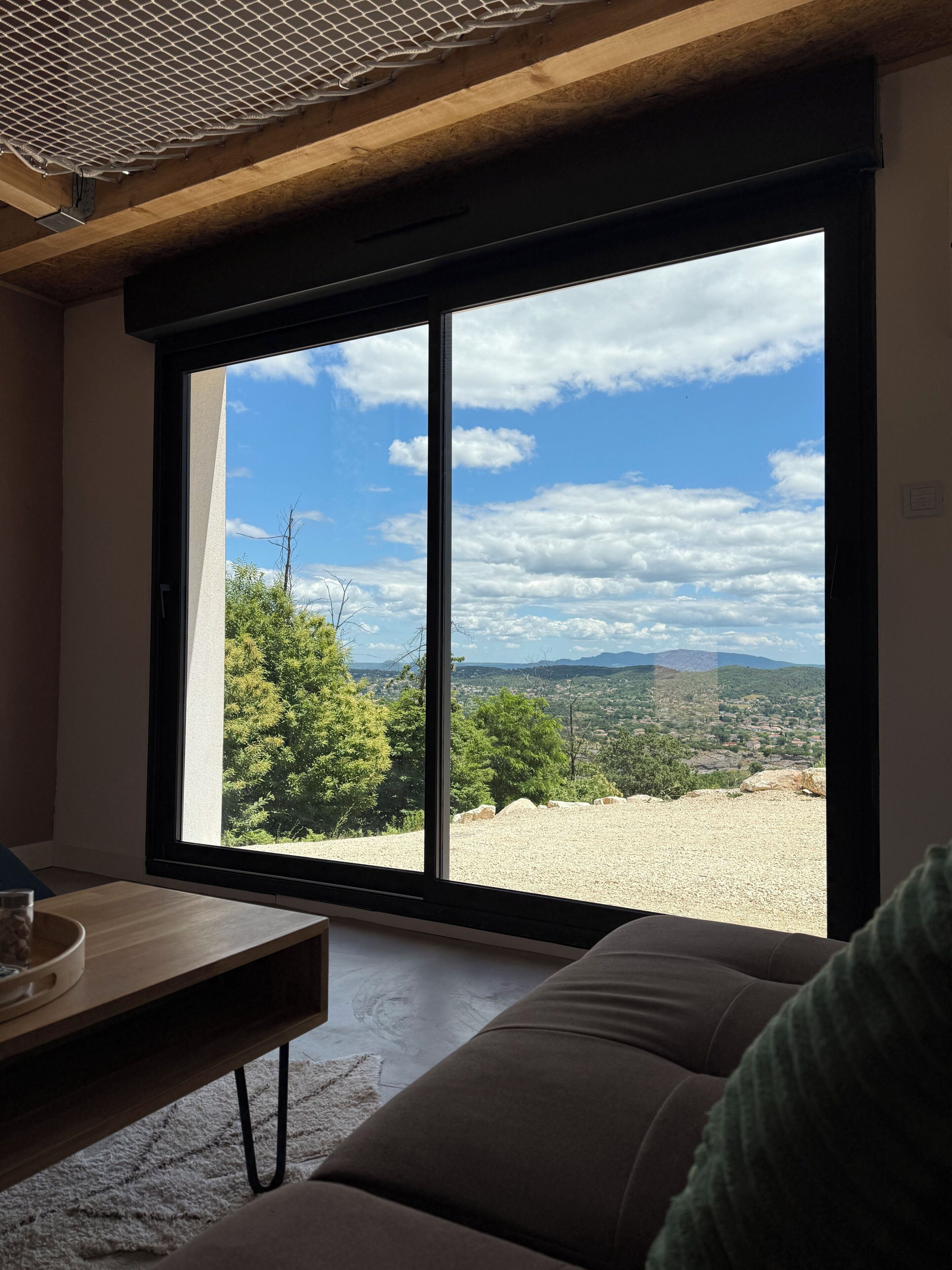 Una habitación con un gran ventanal corredero que da a un espacio exterior con vistas a árboles y colinas distantes.