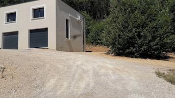 Een modern gebouw met twee garagepoorten, een grindpad en een dichte boomrij in de verte.