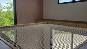A room with a bed frame, a window, and a view of greenery outside.