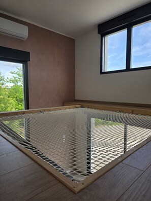 A room with a bed frame, a window, and a view of greenery outside.