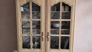 A wooden cabinet with multiple shelves and glass doors, featuring various kitchenware and decorative items.