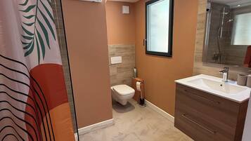 Een badkamer met douche, toilet en wastafel met spiegel.