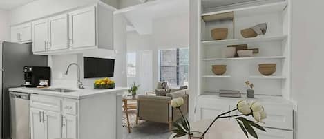 Una cocina moderna con armarios blancos, un comedor con mesa redonda y una sala de estar con sofá y mesa de centro.