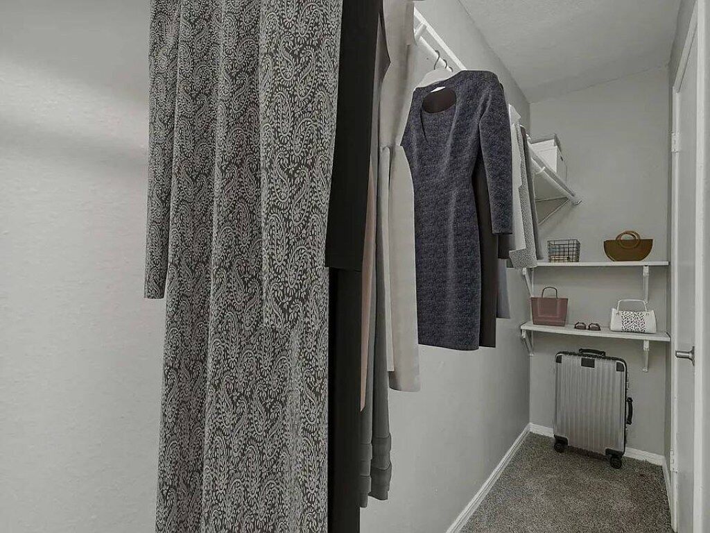 A hallway with a patterned curtain, a grey dress hanging on the wall, and a suitcase on the floor.