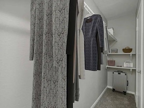 Un pasillo con una cortina estampada, un vestido gris colgado en la pared y una maleta en el suelo.