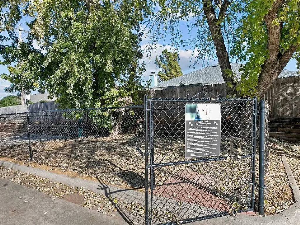 A fenced area with a signboard, trees, and a building in the background.
