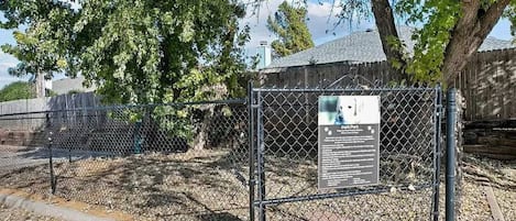 A fenced area with a signboard, trees, and a building in the background.
