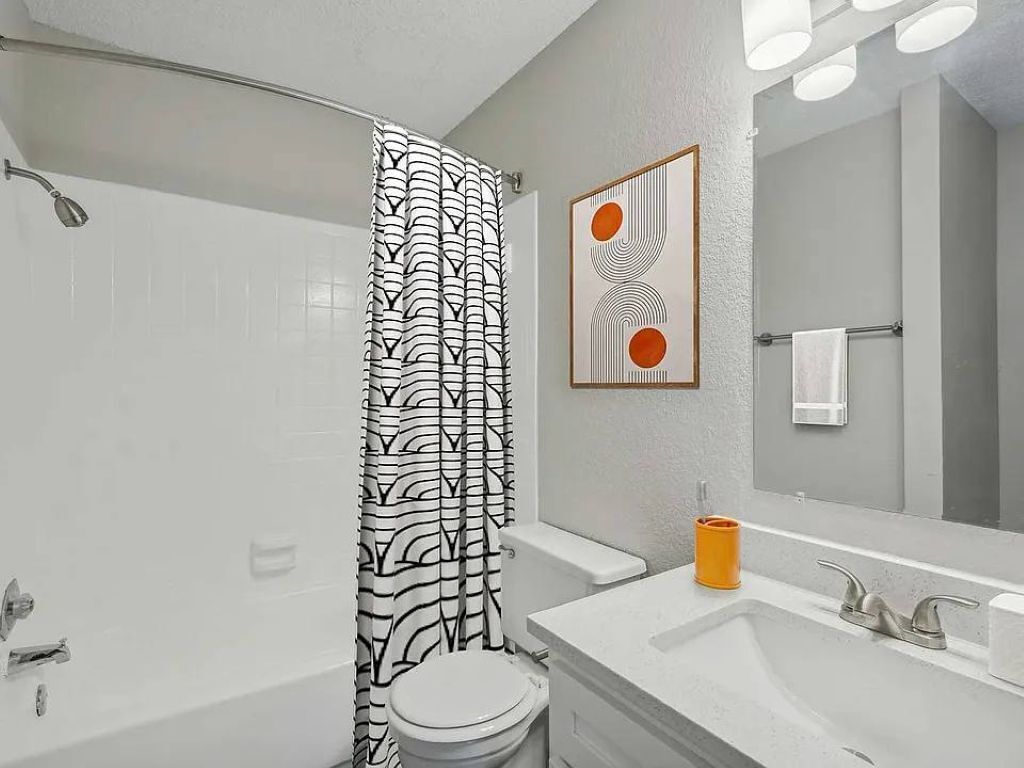 Ein Badezimmer mit Duschvorhang, Toilette, Waschbecken und Spiegel.