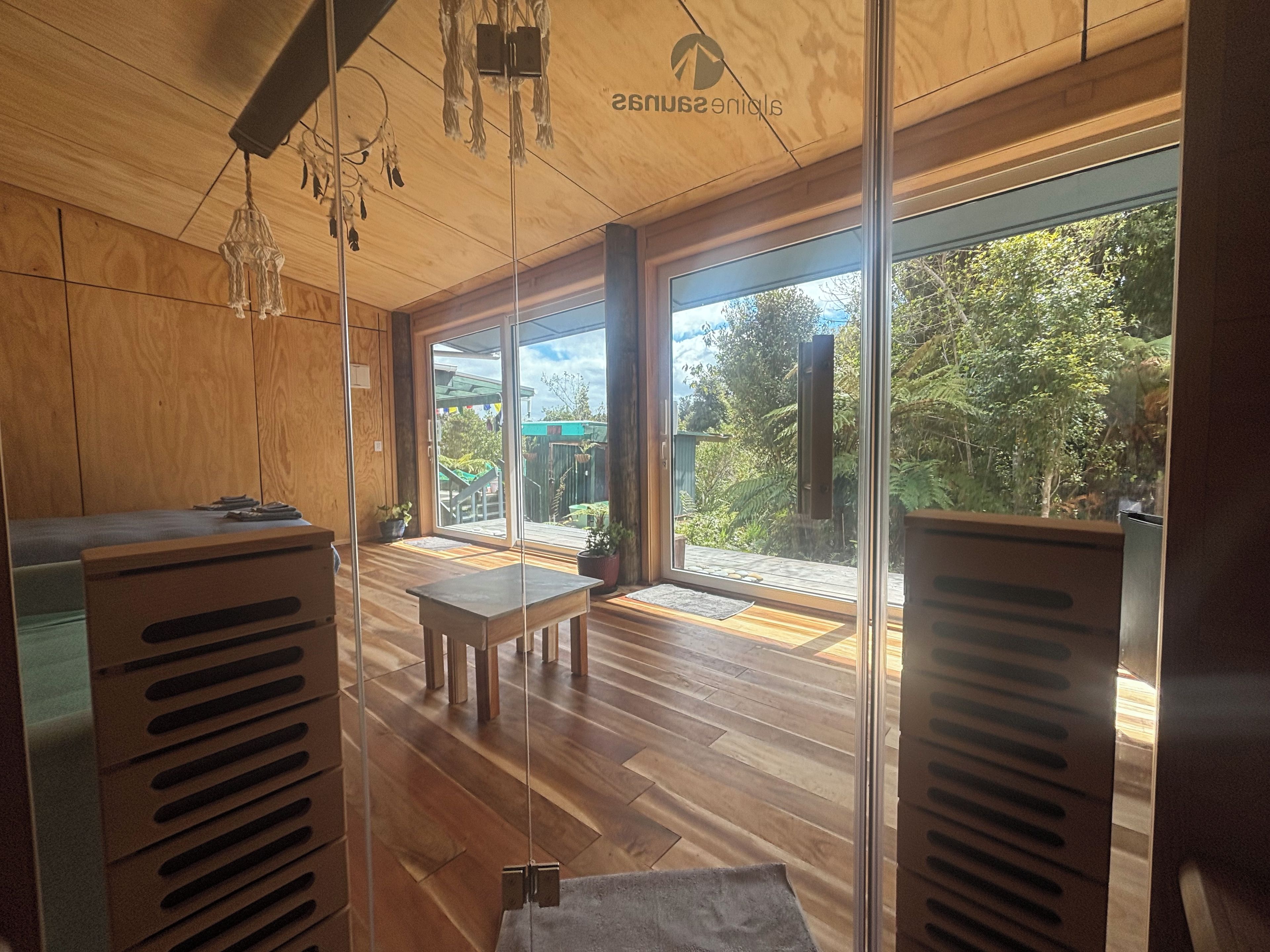 A modern interior with wooden flooring, a dining area, and large windows offering a view of a garden.