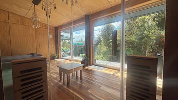 A modern interior with wooden flooring, a dining area, and large windows offering a view of a garden.