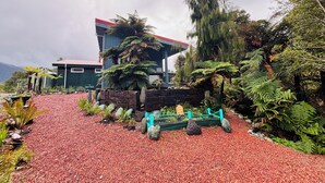 A building with a red roof, surrounded by lush greenery and a gravel path.