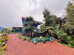 A building with a red roof, surrounded by lush greenery and a gravel path.