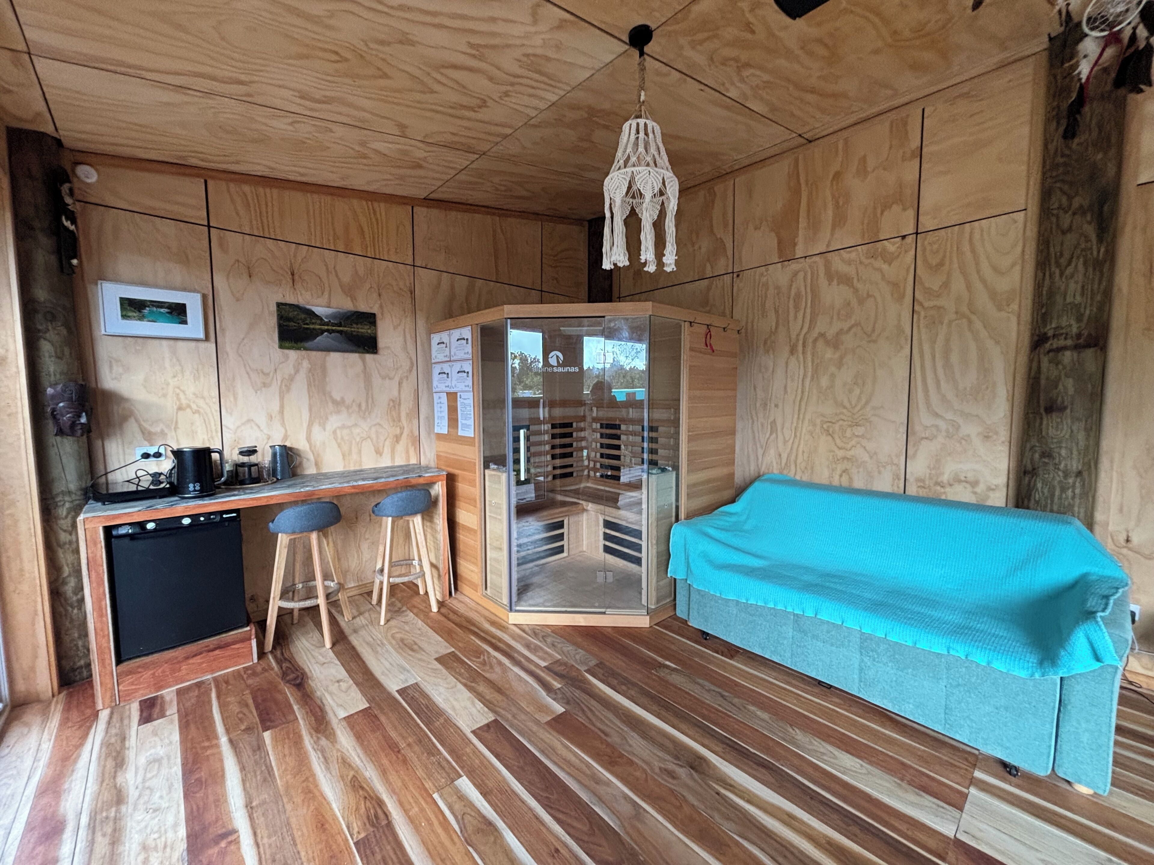 Une pièce avec un plancher en bois, un canapé, un petit coin bar avec des tabourets et un sauna.
