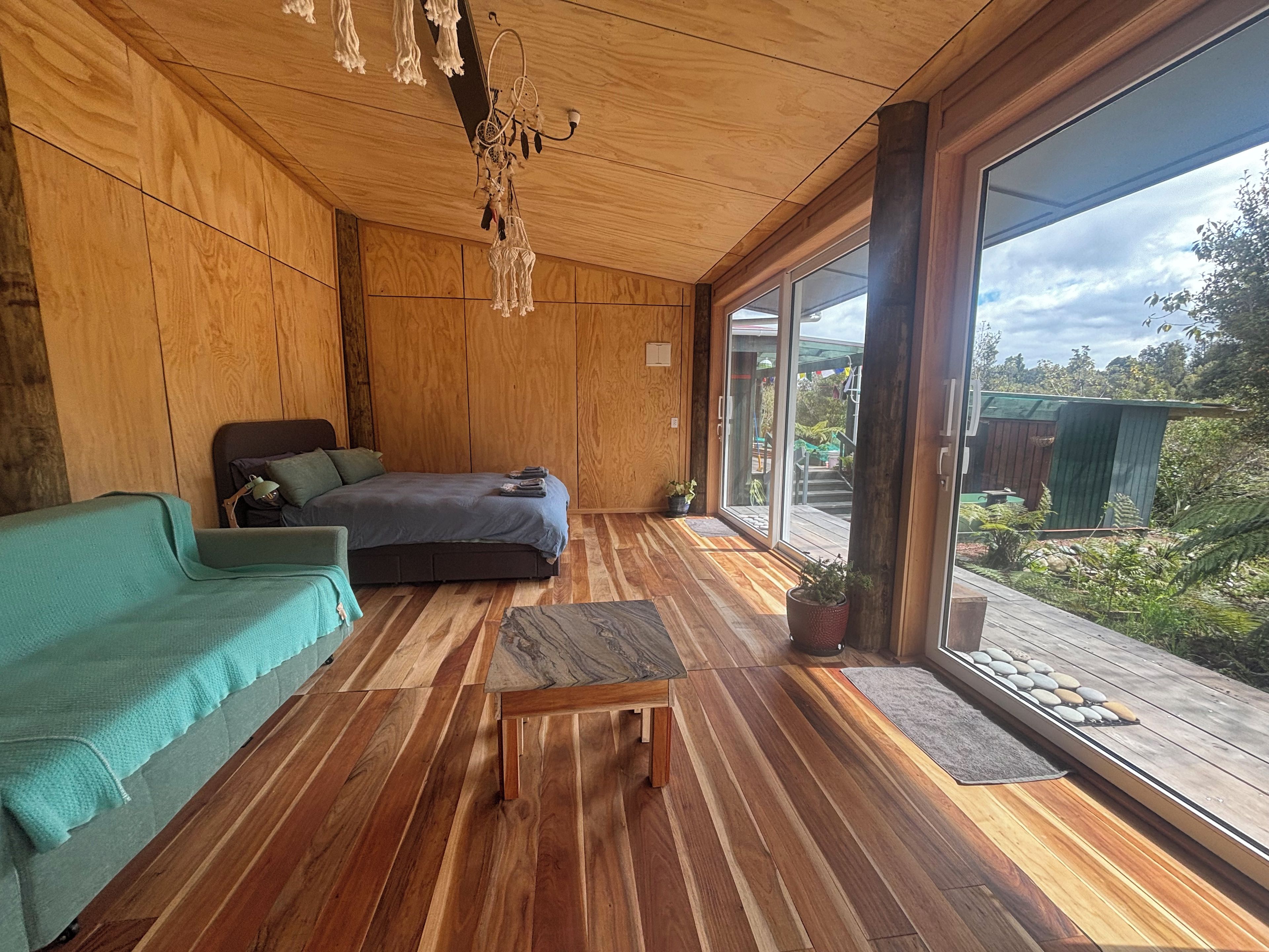 Een kamer met een bed, een groene bank, een houten salontafel en een grote glazen schuindeur die uitkomt op een buitenruimte.