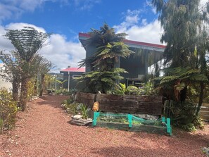 A pathway leading to a building with a red roof, surrounded by lush greenery and a wooden fence.