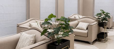 Ein modernes Wohnzimmer mit einem beigen Sofa, einem schwarzen Beistelltisch und einer Topfpflanze.