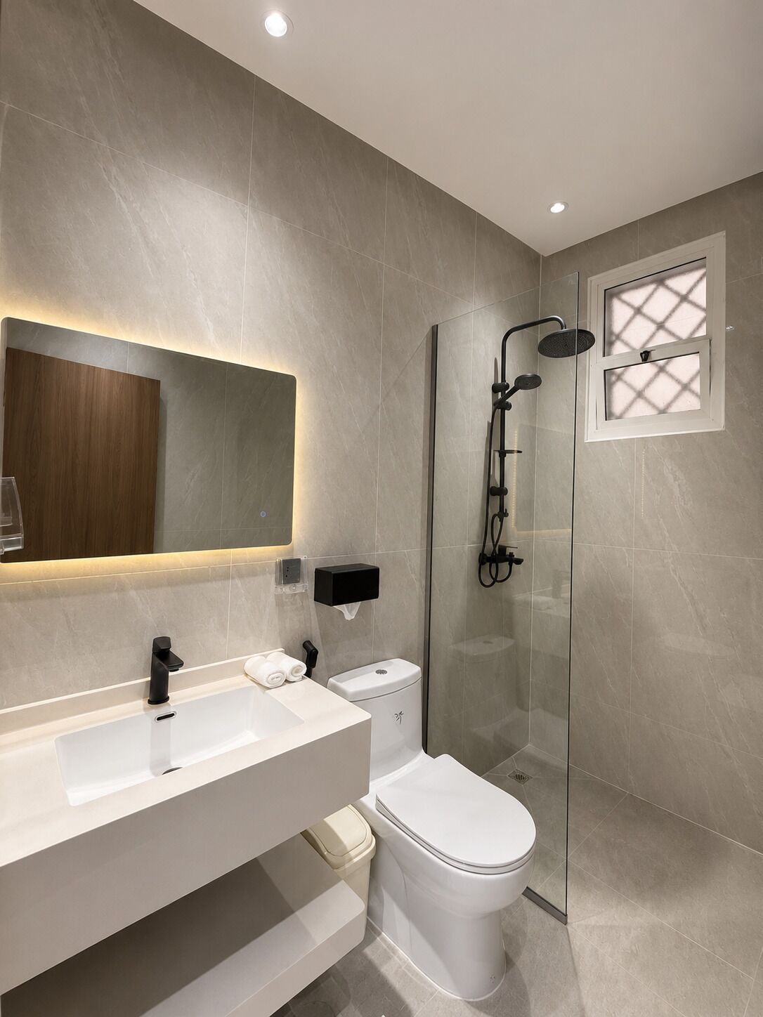 A modern bathroom with a glass-enclosed shower, a large mirror, and a white sink.