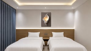 Une chambre d’hôtel moderne avec deux lits, une tête de lit en bois, un éclairage encastré au plafond et une seule œuvre d’art accrochée au mur.