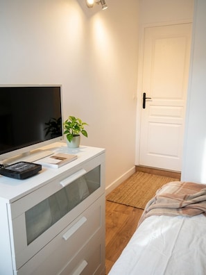 A bedroom with a bed, a bedside table with a TV, a plant, and a door. - Parisian Apart Center—Rue St.Charles,Near Beaugrenelle/ Eiffel Tower—75015 PARIS (Paris15)