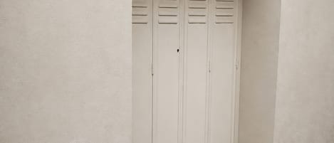 A closed door with horizontal louvered panels, a concrete floor, and a plain wall.