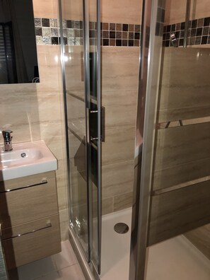 Un baño con cabina de ducha de vidrio, lavabo con grifo y pared con azulejos.