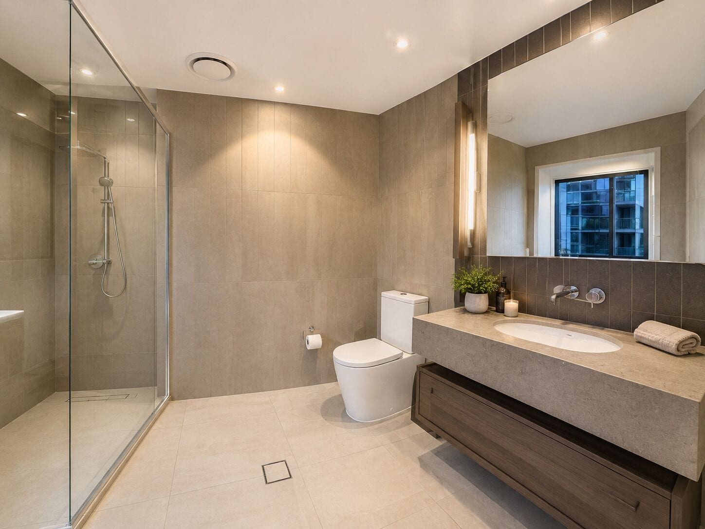 A modern bathroom with a glass shower enclosure, a toilet, a sink with a vanity, and a window providing a view of the outside.