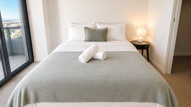 A hotel room with a bed, a nightstand, a lamp, and a view of the city through a large window. - The Riverglass Retreat | Brisbane Skyline Escape (Brisbane City)