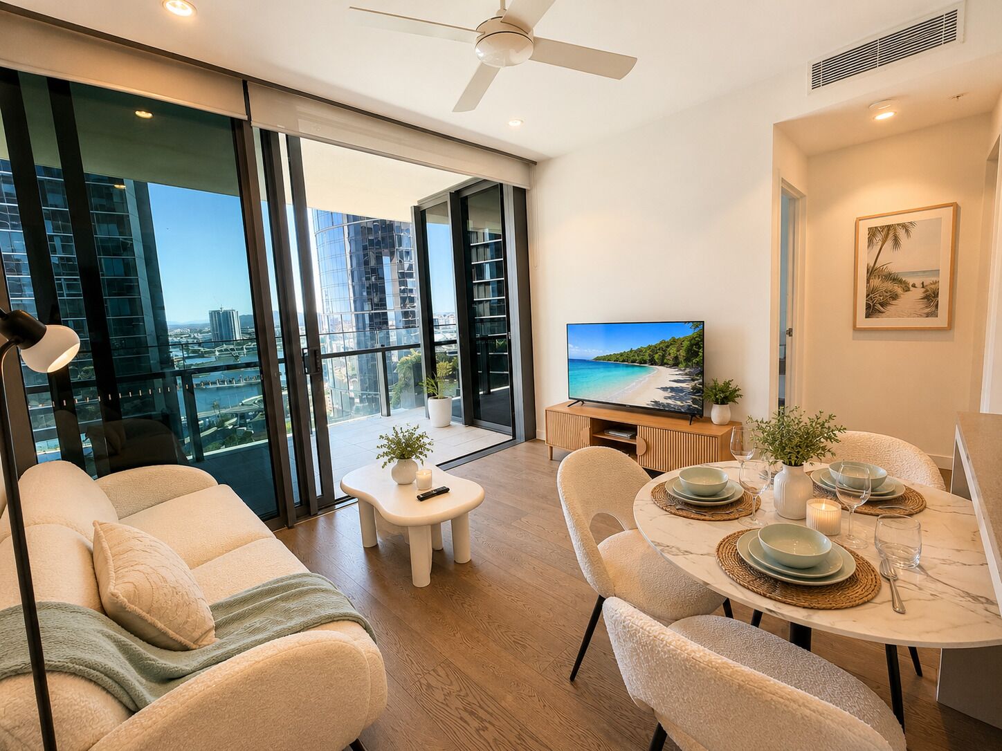 A modern living room with a sofa, a dining table set for four, a television, and a city view through large windows.