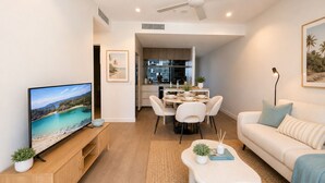 A modern living room with a flat-screen TV, a dining area with a table and chairs, a sofa, and a ceiling fan. - The Riverglass Retreat | Brisbane Skyline Escape (Brisbane City)