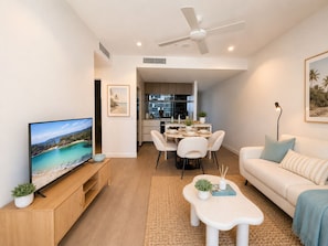 Un salon moderne doté d’un téléviseur à écran plat, d’un coin repas avec une table et des chaises, d’un canapé et d’un ventilateur de plafond.
