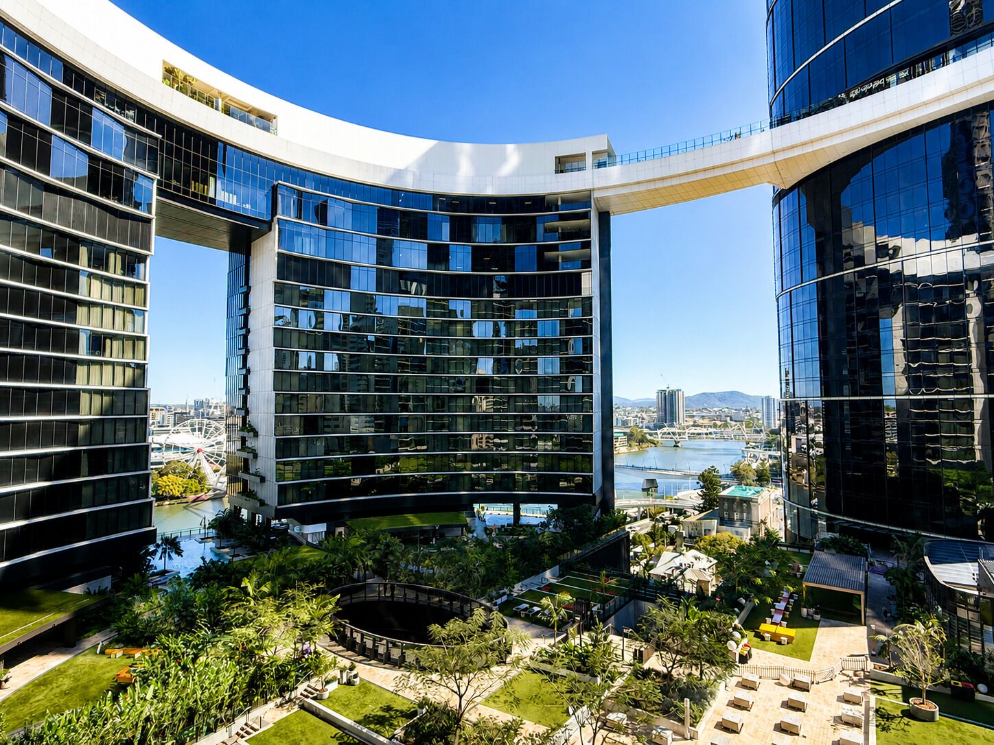 A modern building with a curved glass facade, a rooftop garden, and a view of a river.