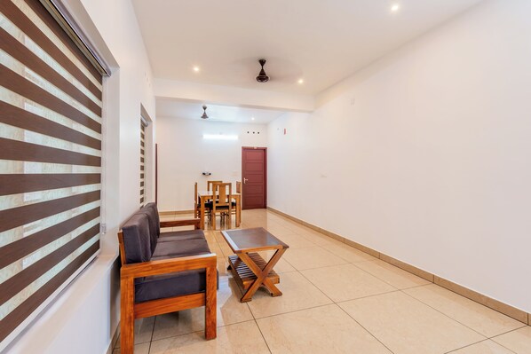 Un interior moderno con un sofá, una mesa de madera y un comedor en una habitación luminosa con paredes blancas y suelo de baldosas.