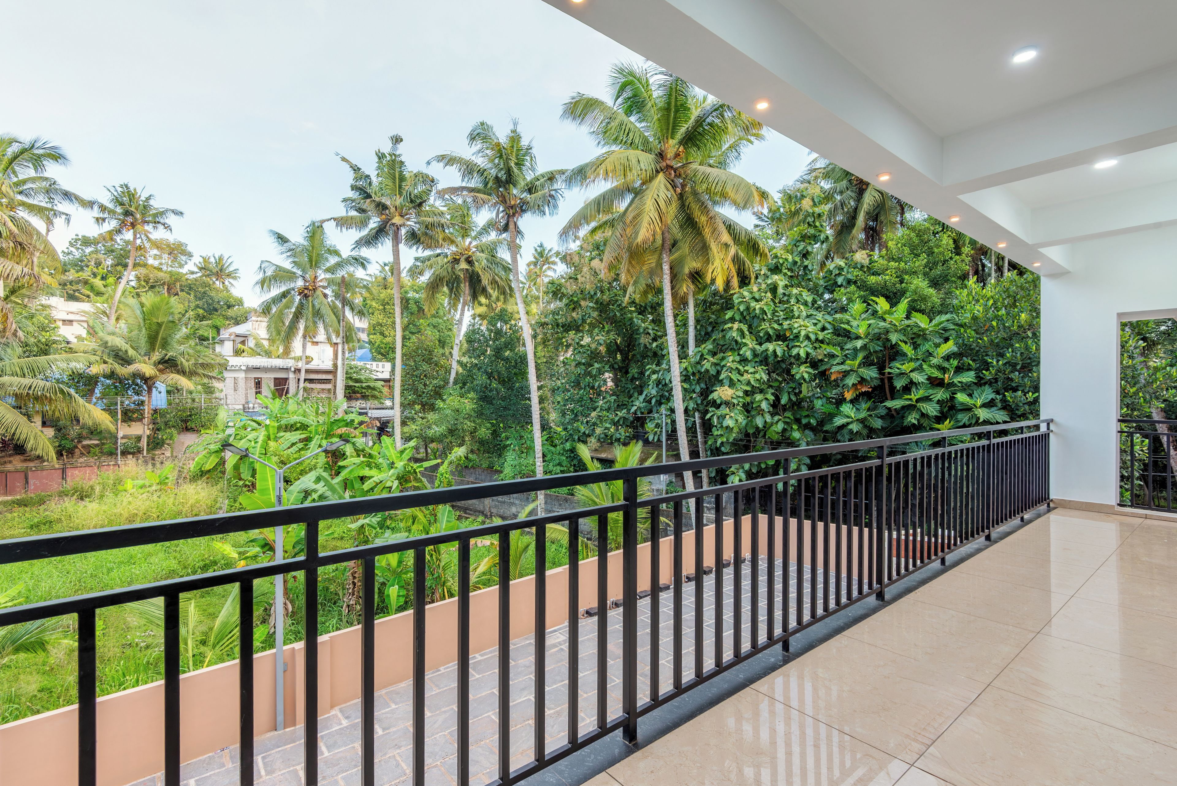 A corridor with a view of a lush garden with palm trees and a tiled floor.