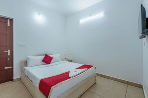 Una habitación de hotel con una cama, una mesita de noche, un televisor en la pared y una puerta.