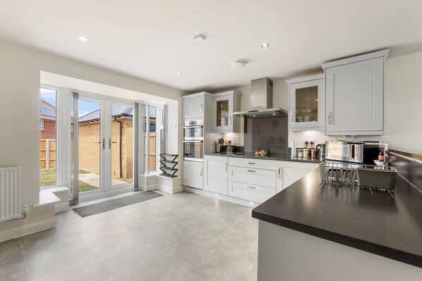 A modern kitchen with sliding glass doors leading to a patio, built-in appliances, and a black countertop. - Five separate bedrooms on a quiet cul-de-sac in NR4, minutes from the A47. A room each for a team of five, or sleeps up to 9 when couples share. Open-plan kitchen the full depth of the house, driveway parking for three and 293 Mbps WiFi. (Norwich)