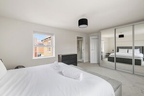A bedroom with a bed, a walk-in closet, and a view of the outside. - Five separate bedrooms on a quiet cul-de-sac in NR4, minutes from the A47. A room each for a team of five, or sleeps up to 9 when couples share. Open-plan kitchen the full depth of the house, driveway parking for three and 293 Mbps WiFi. (Norwich)