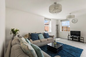 A modern living room with a sofa, coffee table, and a TV. - Five separate bedrooms on a quiet cul-de-sac in NR4, minutes from the A47. A room each for a team of five, or sleeps up to 9 when couples share. Open-plan kitchen the full depth of the house, driveway parking for three and 293 Mbps WiFi. (Norwich)