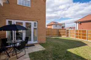 A backyard with a patio table and chairs, a wooden fence, and a brick house. - Five separate bedrooms on a quiet cul-de-sac in NR4, minutes from the A47. A room each for a team of five, or sleeps up to 9 when couples share. Open-plan kitchen the full depth of the house, driveway parking for three and 293 Mbps WiFi. (Norwich)