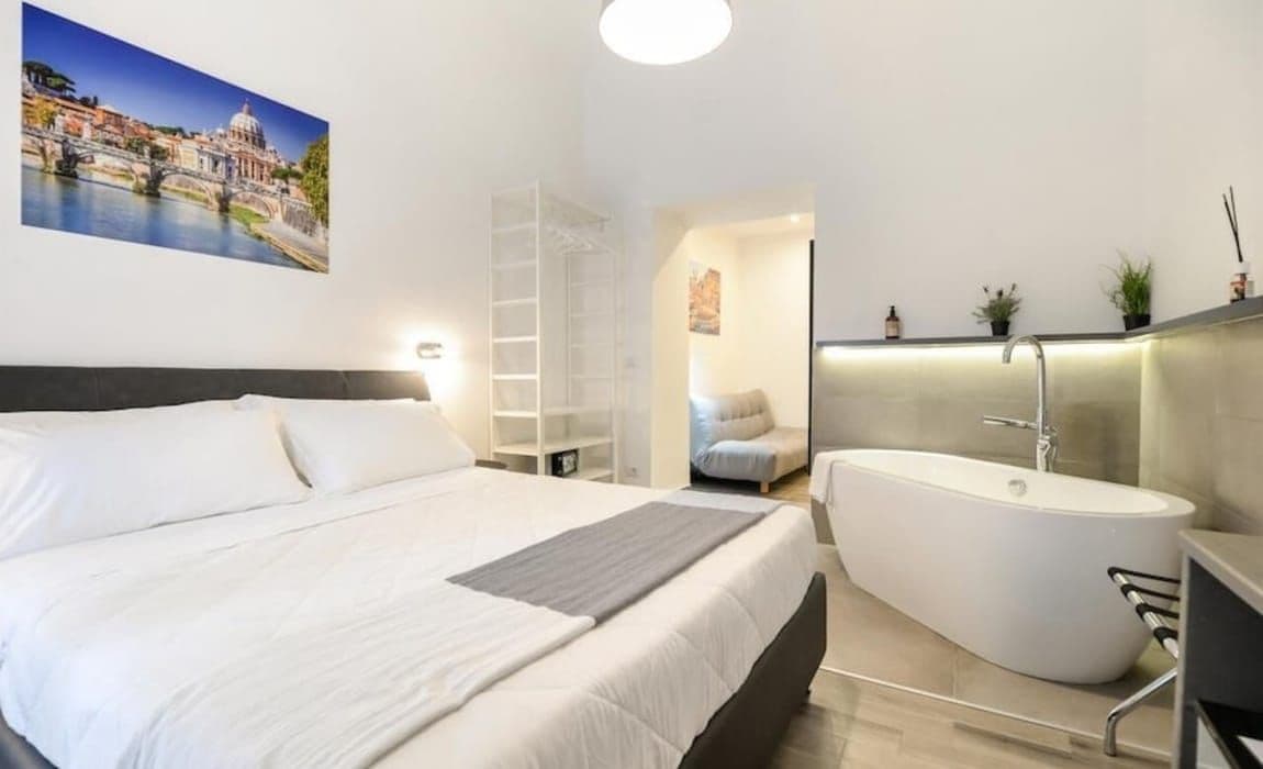Ett modernt sovrum med en stor säng, en rymlig klädkammare, ett badrum med ett fristående badkar och en tavla med en stadsbild på väggen.