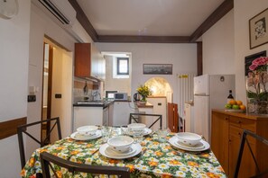 A dining area with a table set for four, a kitchen in the background, and a clock on the wall. - San Frediano Central Stay (Florence)