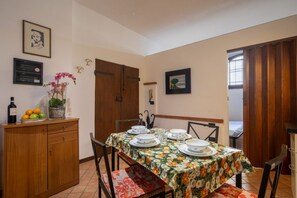 A dining area with a table set for four, a wooden cabinet with fruit and a bottle, and a door with a picture frame. - San Frediano Central Stay (Florence)