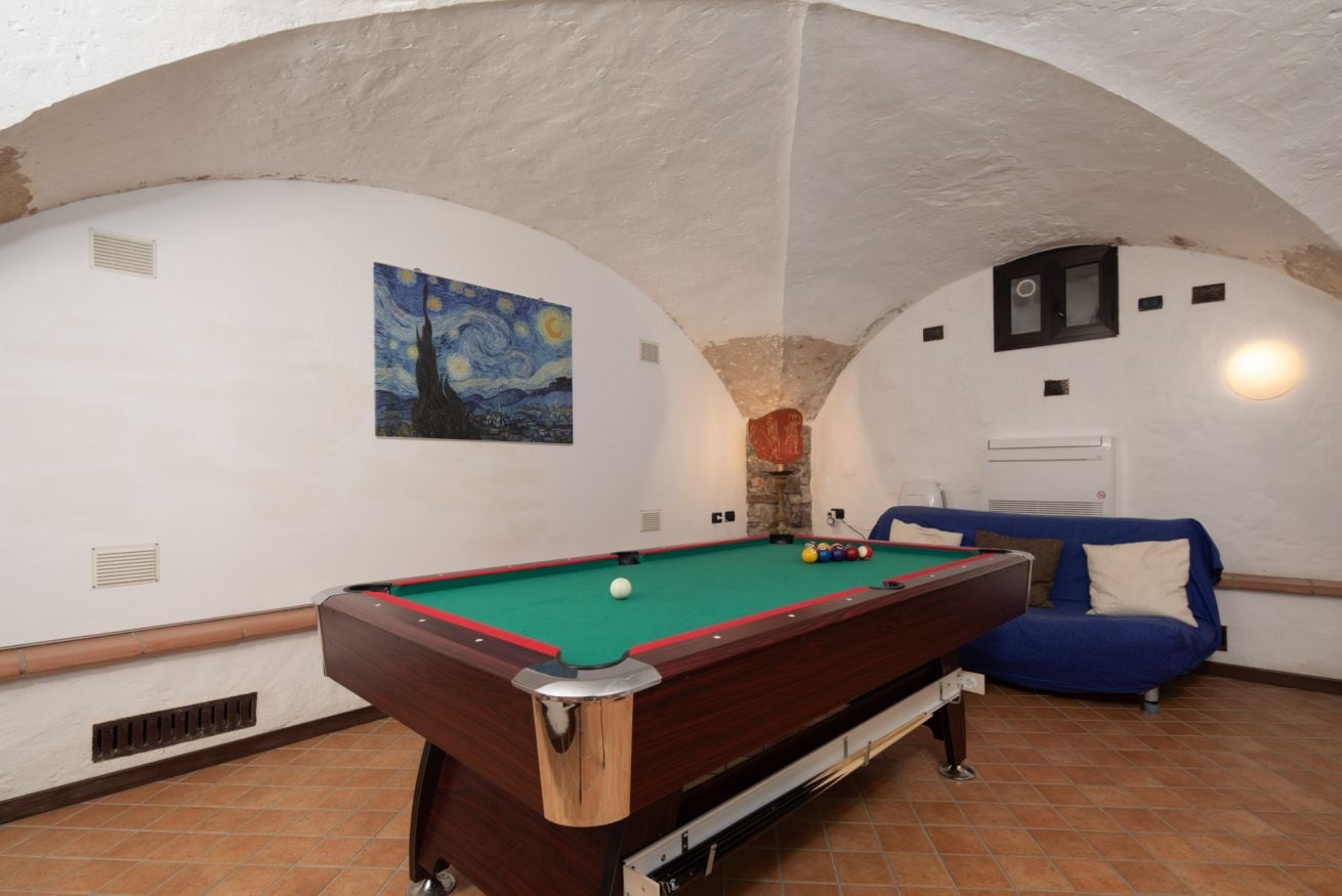 A pool table in a room with a blue sofa, a painting on the wall, and a stone fireplace.